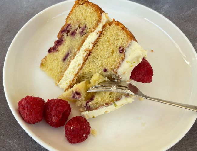 slice of raspberry and lime cake on a plate with fresh raspberries
