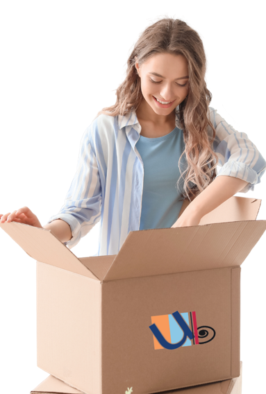 A smiling woman with long, wavy hair is opening a cardboard box. She is wearing a blue shirt under a white and blue striped button-up shirt. The Totally Awesome Tees Subscription Box from Unboxing the Bizarre has a colorful, abstract logo on the front. The background is white.